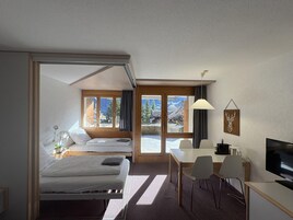 Quarto de hotel com cama, escrivaninha, cadeira, televisão e janelas amplas.