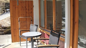 Een terras met een tafel en twee stoelen, een houten deur en een groot raam.