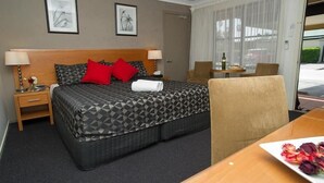 A hotel room with a bed, bedside tables, a chair, a table with a plate of flowers, and a window with curtains. - Grapevine Motel (Denman)