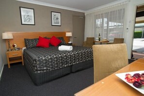 Una camera d'albergo con un letto, comodini, una sedia, un tavolo con un piatto di fiori e una finestra con tende.