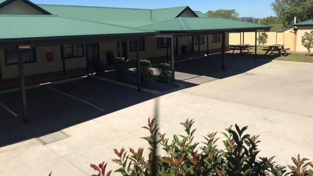 A building with a green roof, covered outdoor seating, and a parking lot. - Grapevine Motel (Denman)