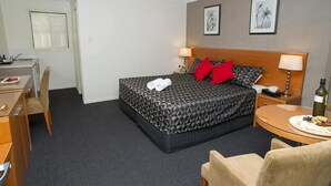 A hotel room with a bed, bedside tables, a desk, and a chair. - Grapevine Motel (Denman)