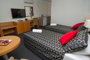 Una camera d'albergo con due letti, una scrivania, una televisione e un angolo cottura.