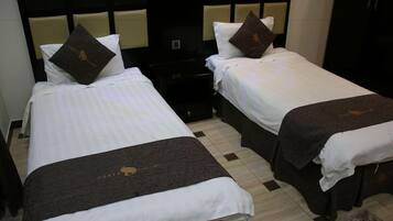 Habitación de hotel con dos camas, cada una con cubrecama blanco y manta marrón oscuro. Hay una pequeña mesa entre las camas y un armario de color oscuro al fondo.