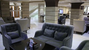 Um hall com sofás, uma mesa de centro e uma escadaria ao fundo.
