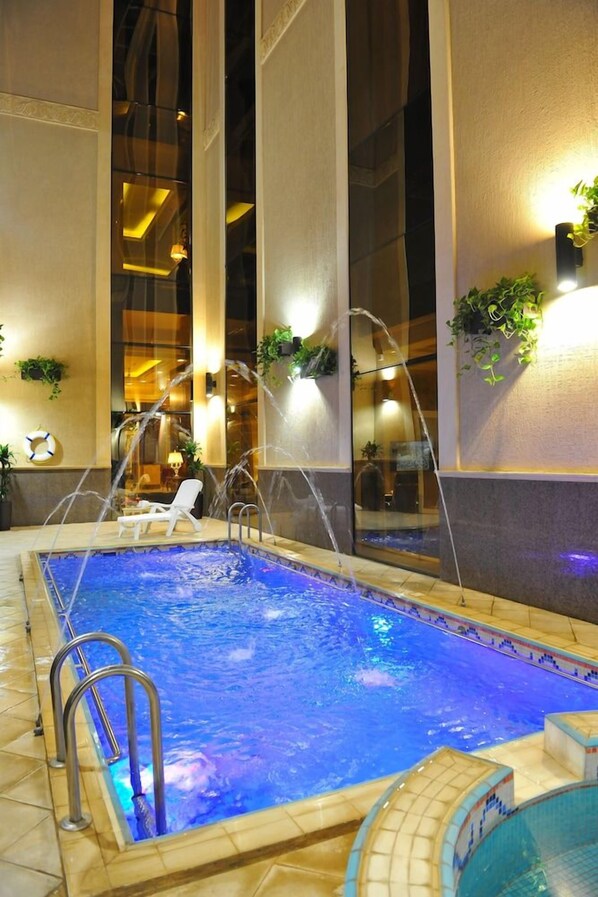 An indoor swimming pool with a clear water feature, surrounded by walls with windows and decorative plants. - Suite Inn Hotel (Riyadh)