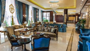 A spacious lobby with a mix of seating options, including sofas and armchairs, a chandelier, and a reception area in the background. - Suite Inn Hotel (Riyadh)