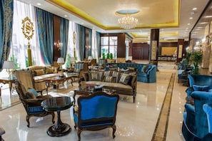 A spacious lobby with a mix of seating options, including sofas and armchairs, a chandelier, and a reception area in the background. - Suite Inn Hotel (Riyadh)