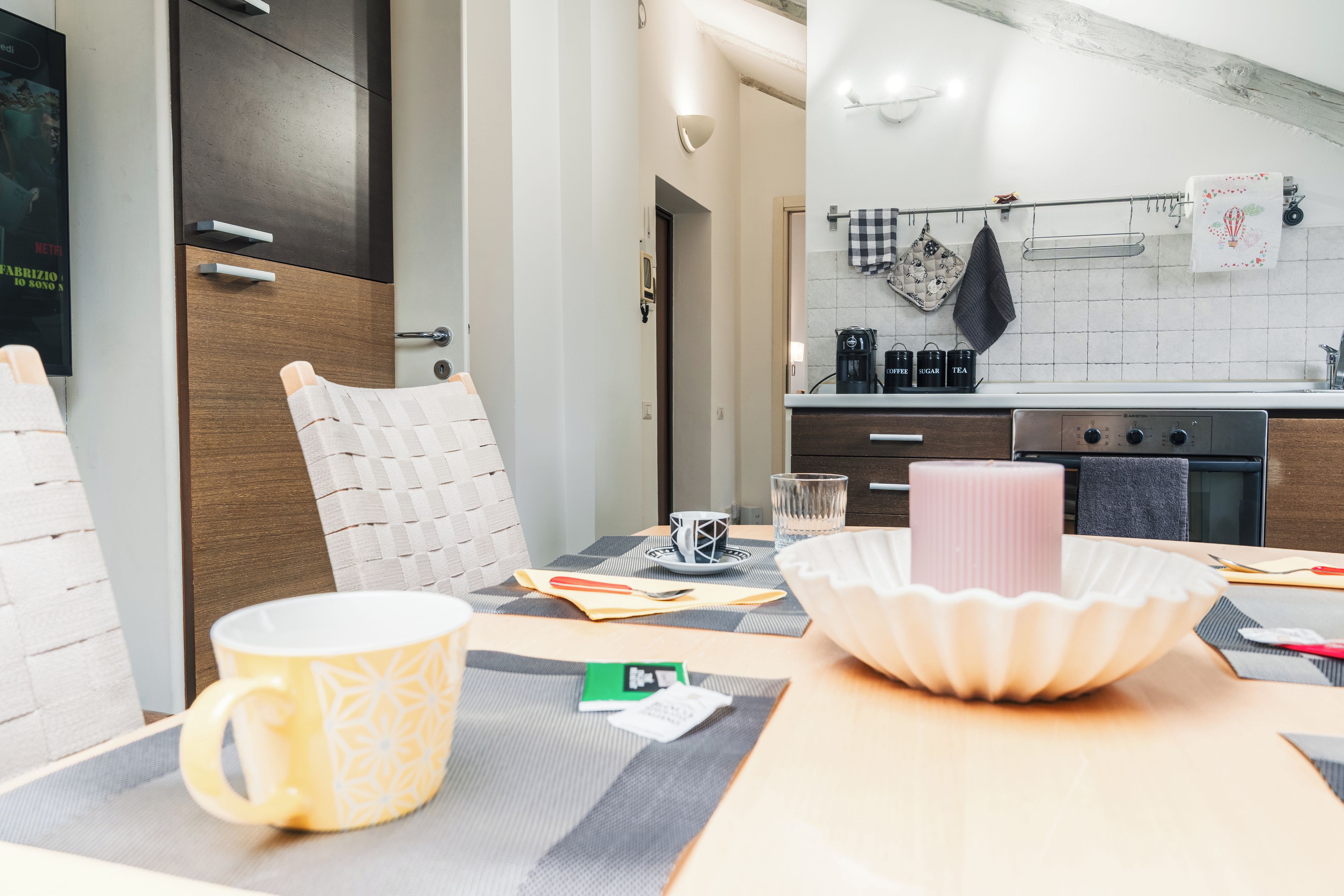 A modern kitchen with a dining area, including a table with a placemat, a candle, and a coffee machine.