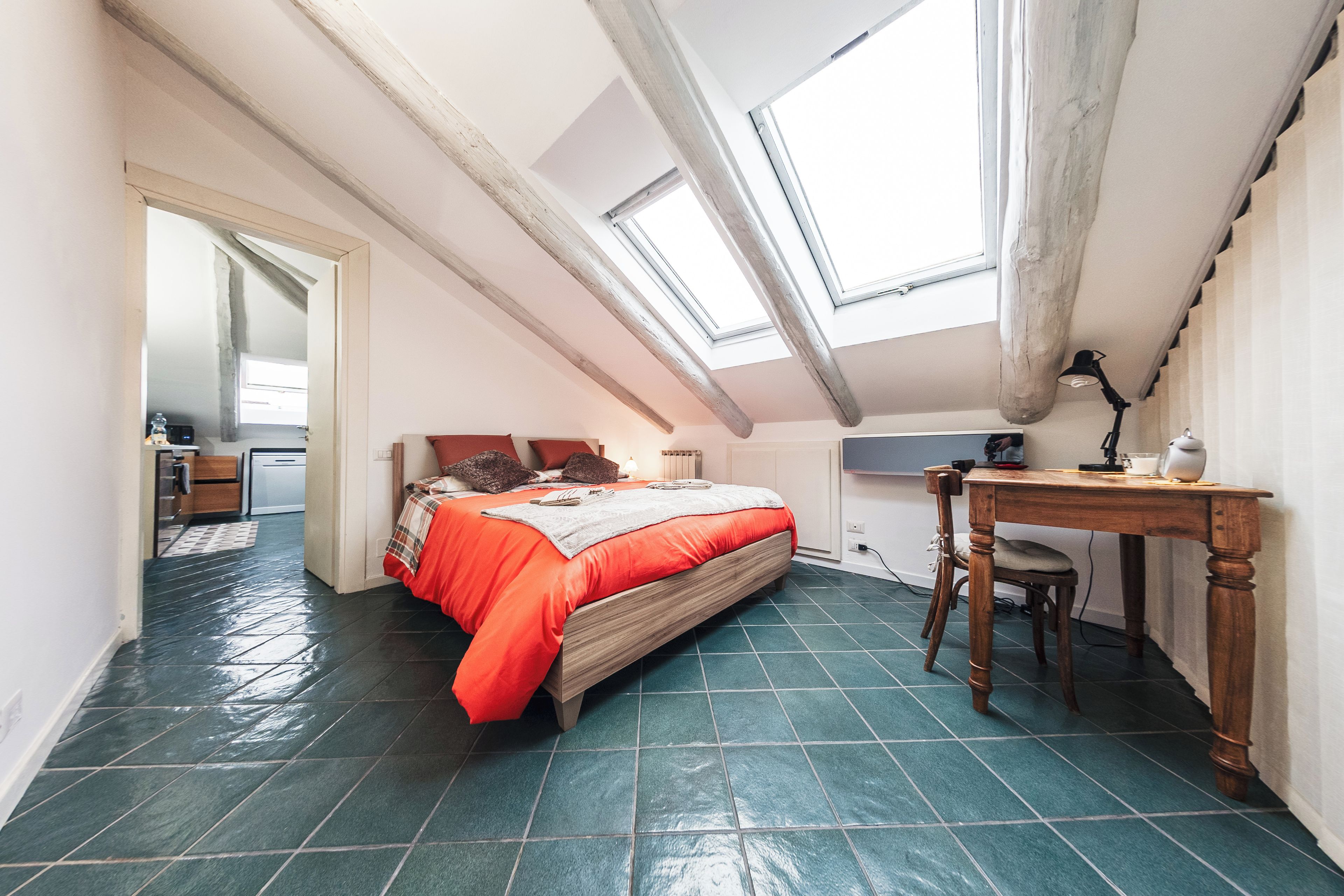 Ein Schlafzimmer mit schrägverdeckter Decke, einem Bett, einem Schreibtisch und einem Stuhl.