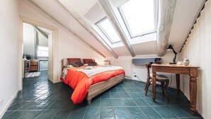 A bedroom with a skylight, a bed with red bedding, a desk, and a chair. - Vrbo Property (Torino)