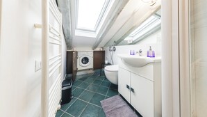 A compact bathroom with a skylight, a washing machine, a toilet, and a sink. - Vrbo Property (Torino)