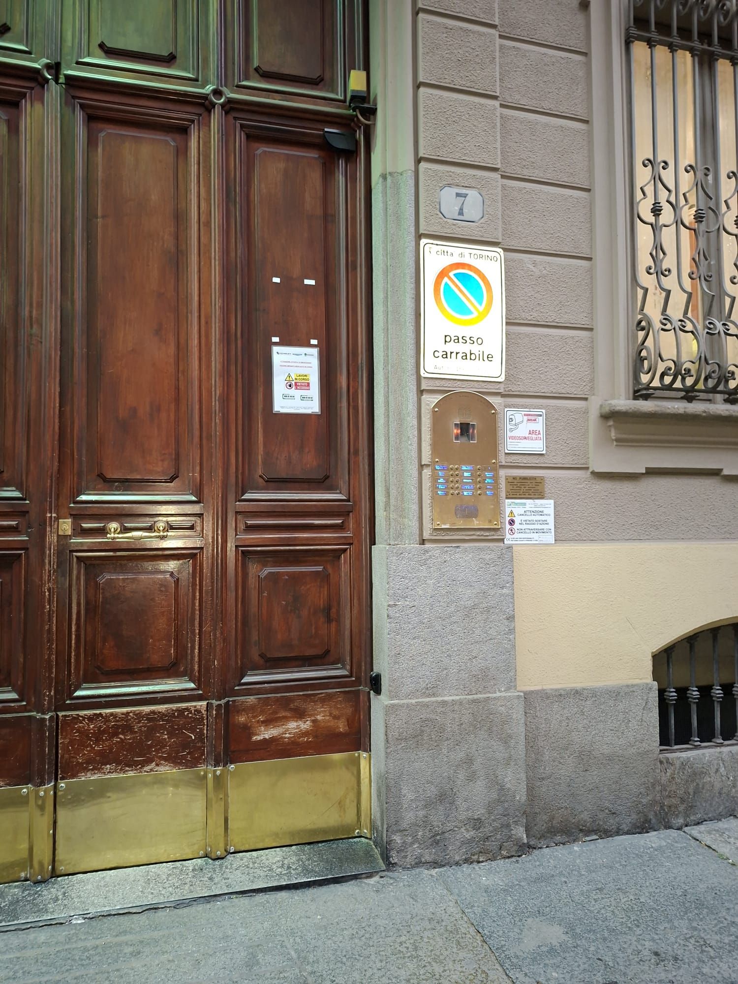 Una porta in legno con una soglia in ottone, un segnale di divieto di parcheggio e un sistema di citofono di sicurezza.