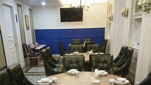 Un espace repas avec des tables et des chaises rondes, un téléviseur à écran plat fixé au mur et un lustre.