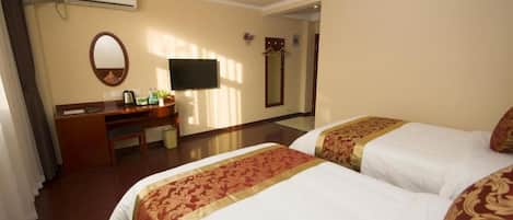 A hotel room with two beds, a desk, a television, and an air conditioning unit.