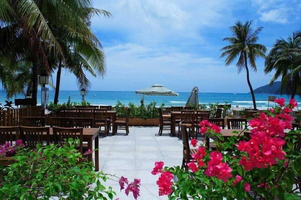 An outdoor seating area with wooden tables and chairs, a view of the ocean, and tropical plants. - South China (Sanya)