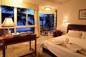 A hotel room with a bed, a desk with a lamp, a chair, and a view of palm trees through the window. - South China (Sanya)