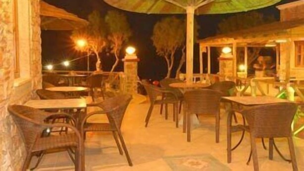 An outdoor seating area with wicker chairs and tables, surrounded by stone walls and umbrellas. - Panteli Beach (Leros)