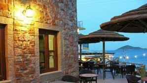 An outdoor seating area with stone walls and tables, overlooking a body of water. - Panteli Beach (Leros)