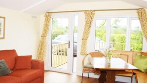 A room with a sofa, a dining table, and a view through a sliding door to an outdoor area. - Dove Meadow (Uttoxeter)