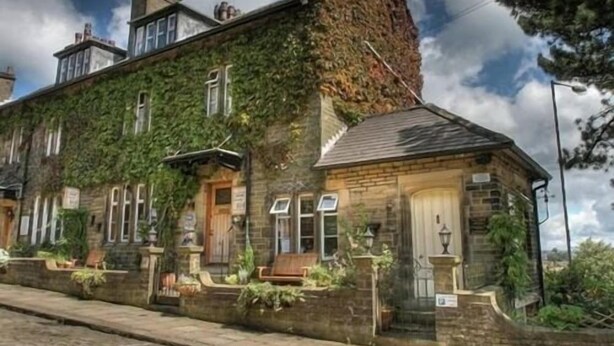 A stone building with ivy-covered walls, a chimney, and a small porch with a bench. - The Old Registry Haworth - Guest House (Keighley)