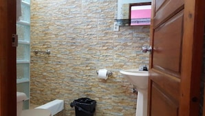 A bathroom with a stone wall, a sink, a toilet, and a trash bin. - Anchorage Resort (Caye Caulker)