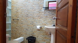 A bathroom with a stone wall, a sink, a toilet, and a trash bin. - Anchorage Resort (Caye Caulker)