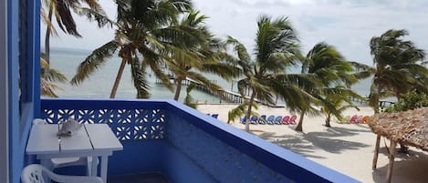 A balcony with a view of a beach, palm trees, and a pier.
