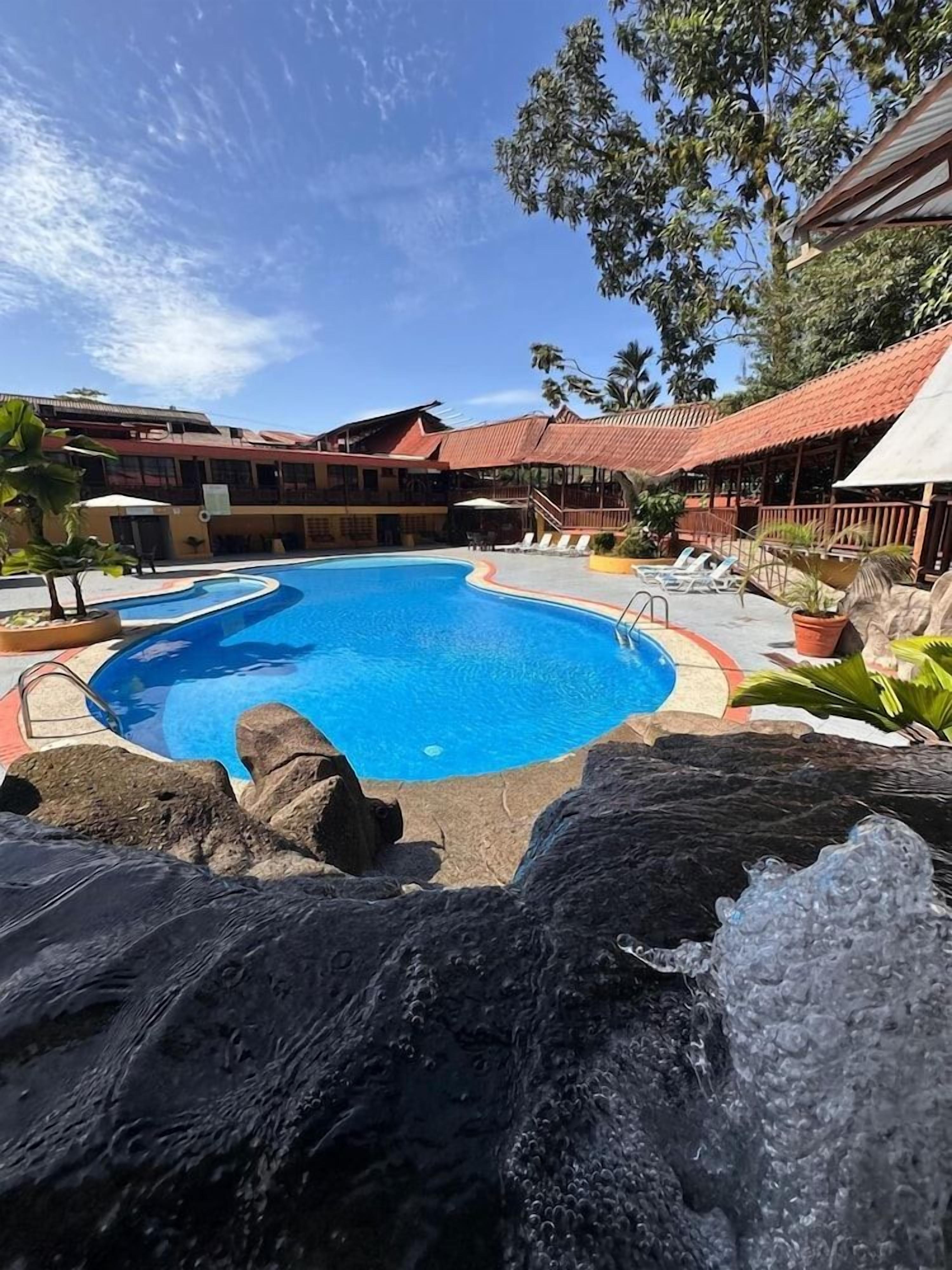 A swimming pool with a circular shape, surrounded by a poolside area with lounge chairs and a rock formation in the foreground.