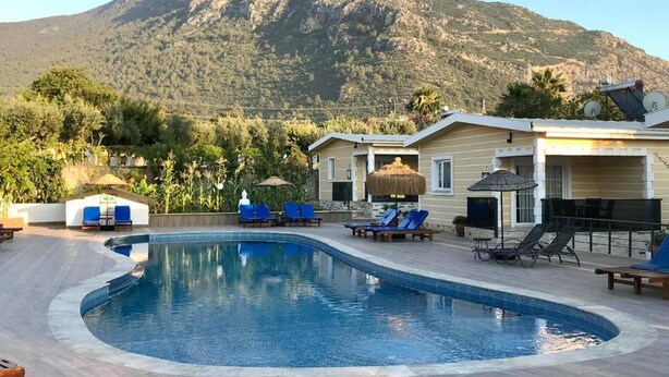 A swimming pool with lounge chairs and a mountain in the background. - Erkan Tumen Yalcin Hotel (Fethiye)