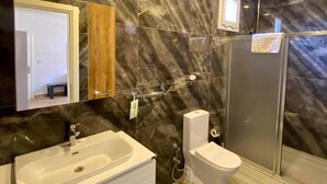 A bathroom with a marble wall, a sink, a toilet, and a shower area. - Erkan Tumen Yalcin Hotel (Fethiye)