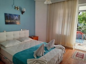 Quarto com cama, mesa de cabeceira, luminária na parede e janela com cortinas.