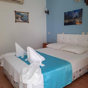 Quarto de hotel com cama, mesa de cabeceira, ar condicionado fixado na parede e duas fotos emolduradas.
