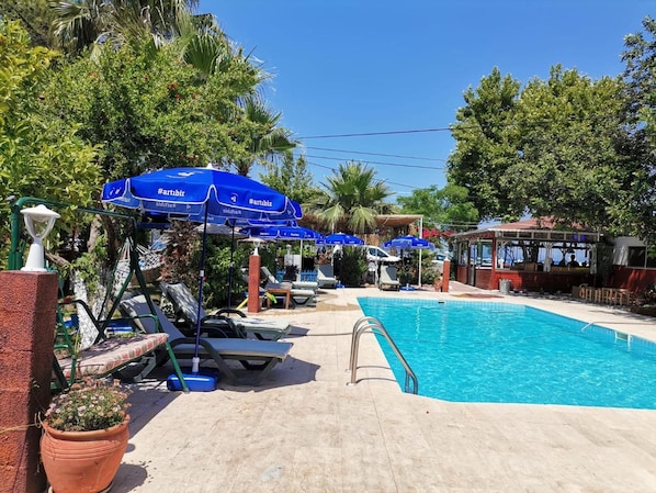 Área da piscina com espreguiçadeiras, guarda-sóis e uma piscina azul cristalina.