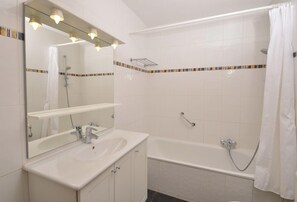 Une salle de bain avec un lavabo blanc, un miroir et une baignoire.