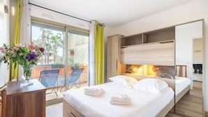 Et hotelværelse med seng, natborde, et skrivebord, en stol og en balkon med udsigt til palmer.