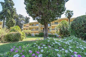 Un immeuble à plusieurs étages doté de balcons, entouré de jardins et d’arbres bien entretenus.