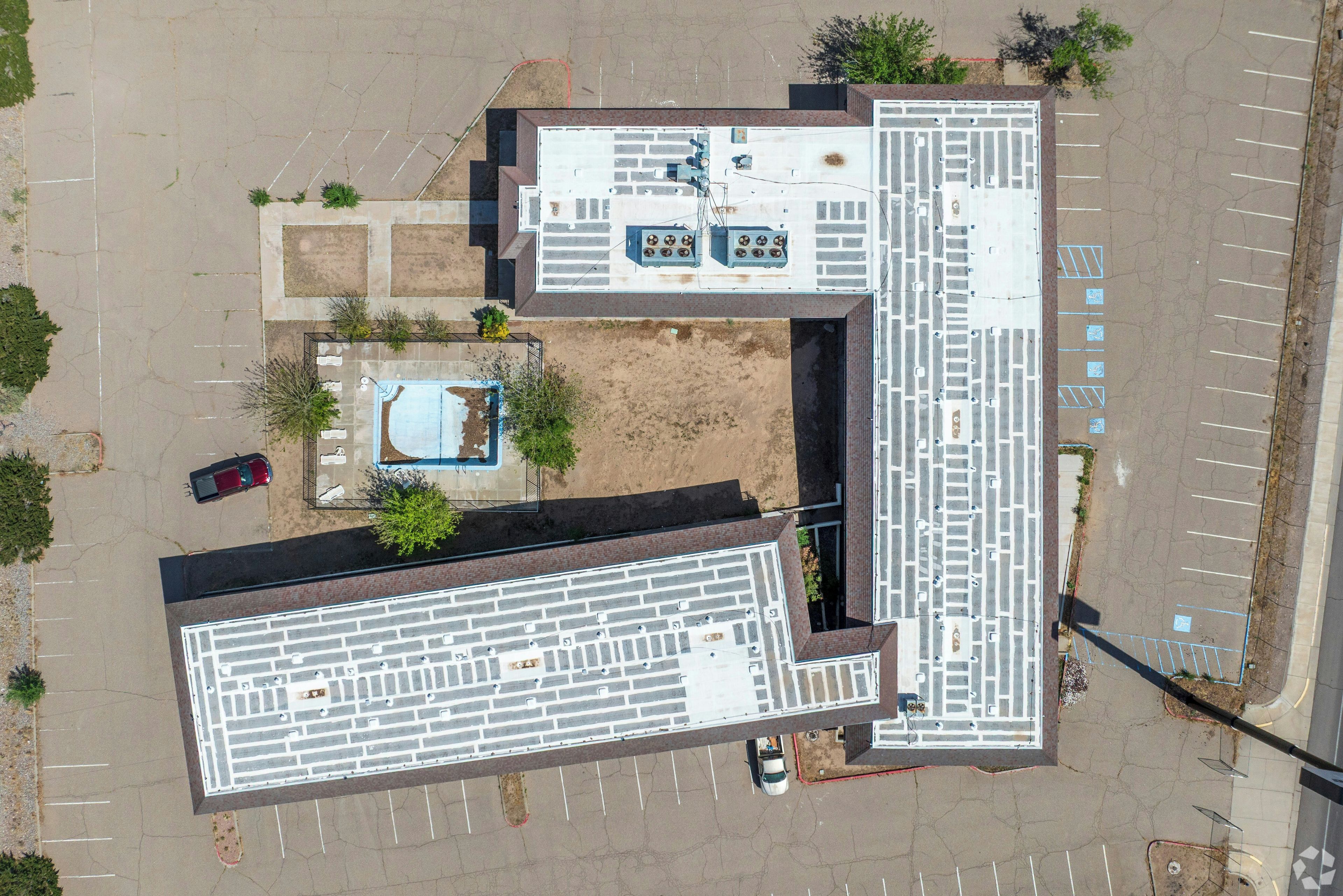 Vue aérienne d’un parking comportant de nombreuses places, d’une piscine et d’un bâtiment à la façade en briques.