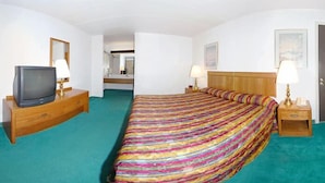 Hotellihuone, jossa on sänky, puinen lipasto ja sen päällä televisio sekä peili.