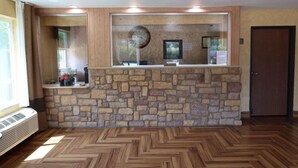 A reception area with a stone wall, wooden floor, and a door to the right. - Scottish Inns & Suites White Settlement (Fort Worth)