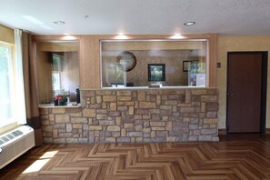 Área de recepção com parede de pedra, piso de madeira e uma porta à direita.