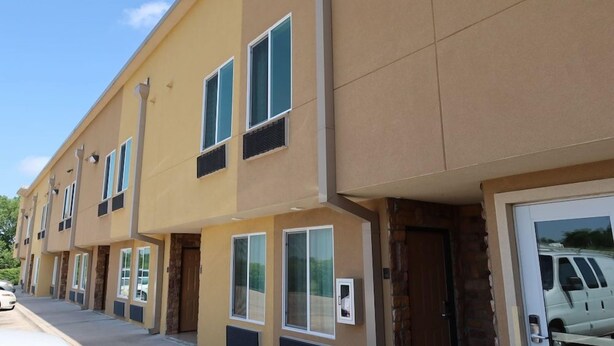 A multi-story building with a beige facade, multiple windows, and a garage door with a vehicle parked inside. - Scottish Inns & Suites White Settlement (Fort Worth)
