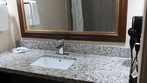 A bathroom with a granite countertop, a white sink, a mirror with a wooden frame, and a towel rack. - Scottish Inns & Suites White Settlement (Fort Worth)