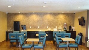 A hotel room with a kitchenette, a dining area with blue chairs and a table, and a patterned wall. - Scottish Inns & Suites White Settlement (Fort Worth)