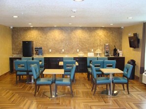 Quarto de hotel com cozinha compacta, área de refeições com cadeiras azuis e mesa, e parede com padrão decorativo.