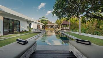 A modern pool area with a clear view of the pool, lounge chairs, and a building with large windows.