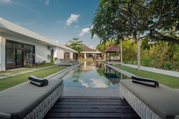 Área de piscina moderna com espreguiçadeiras e vista desimpedida para a casa.