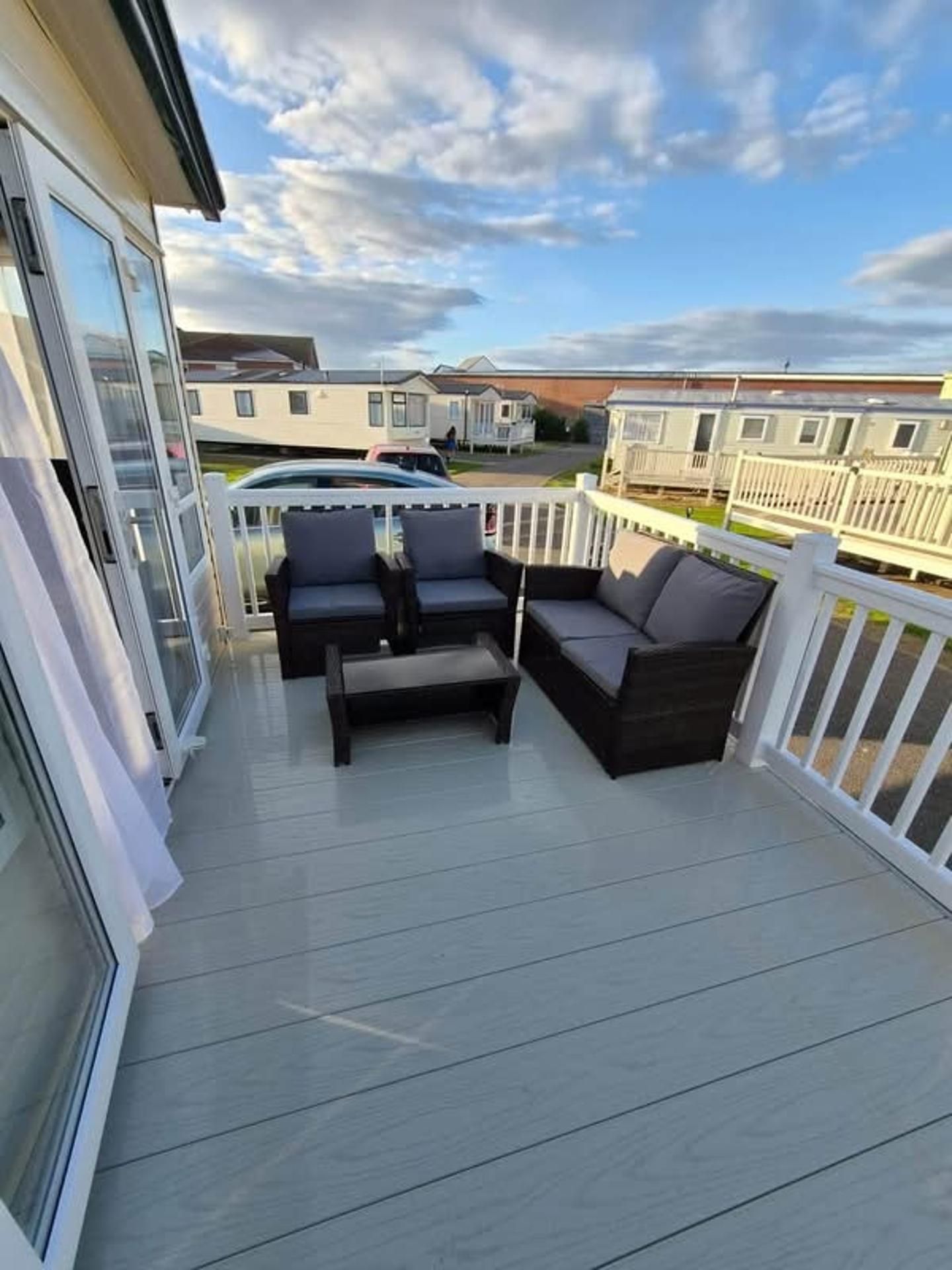 A covered outdoor area with a seating arrangement, a railing, and a view of mobile homes in the background.