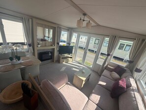 A spacious living area with a sofa, television, and a dining table. - Cabin Sleeps 8 With Parking and Balcony (Skegness)