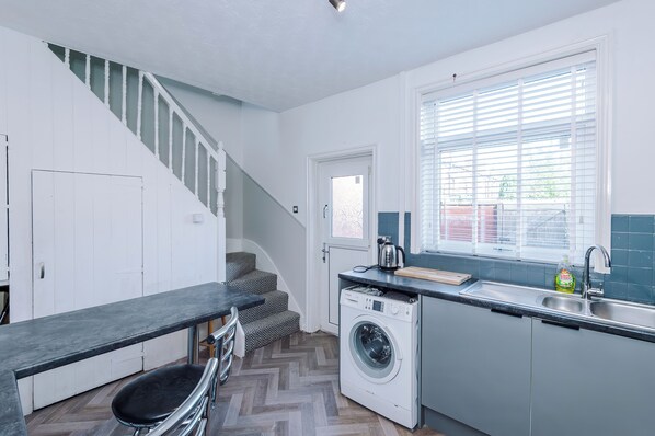 A compact kitchen with a built-in washing machine, a sink, and a window with blinds.